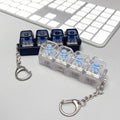 Keychain with transparent case containing small blue objects on a light gray surface with a keyboard in the background.