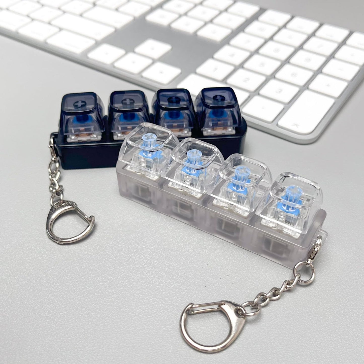 Keychain with transparent case containing small blue objects on a light gray surface with a keyboard in the background.